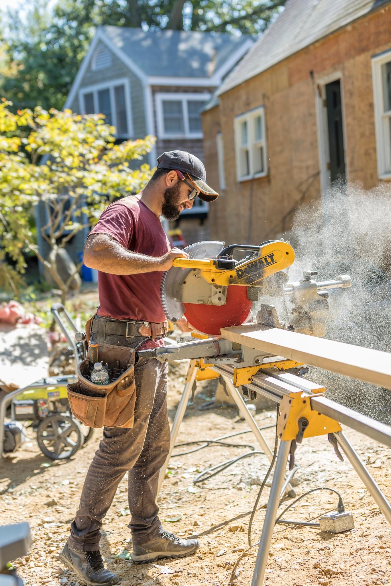 Tekton worker using a chop saw to cut a 2x6 board to length