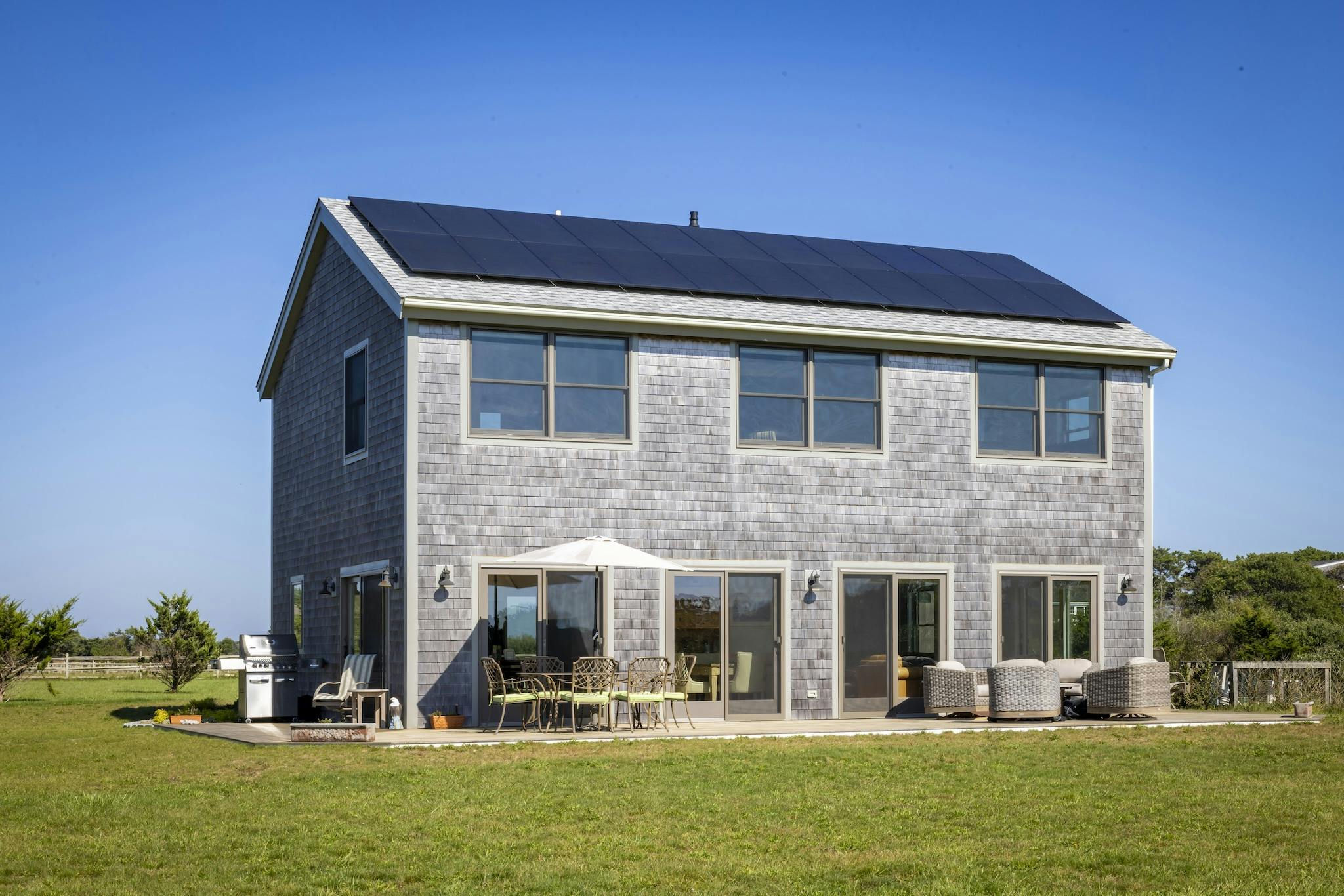 Katama home featuring solar panels, large windows, sliding doors, and a patio